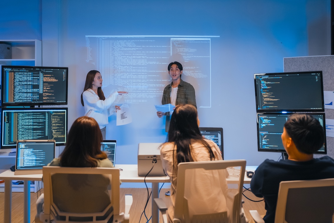 Two developers walking a seated team through code shown on a large screen behind them